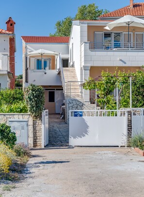 A two-story residential building with a tiled roof, a gated entrance, and a staircase leading to the upper floor. - Seafront apartments Marija with terrace and mooring (Rogoznica)