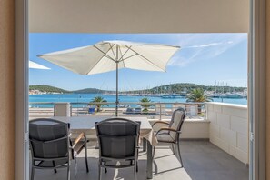 A balcony with a table and chairs, a large umbrella, and a view of the sea and boats. - Seafront apartments Marija with terrace and mooring (Rogoznica)