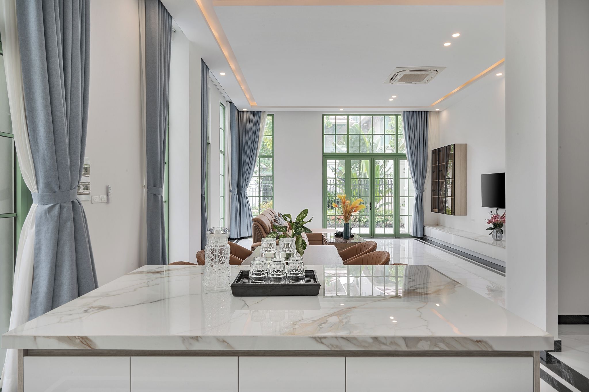 A modern living room with a marble island, large windows, a sofa, and a TV mounted on the wall.
