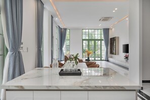 A modern living room with a marble island, large windows, a sofa, and a TV mounted on the wall. - Elyday Villa - Bai Khem Beach, Phu Quoc (Phu Quoc)