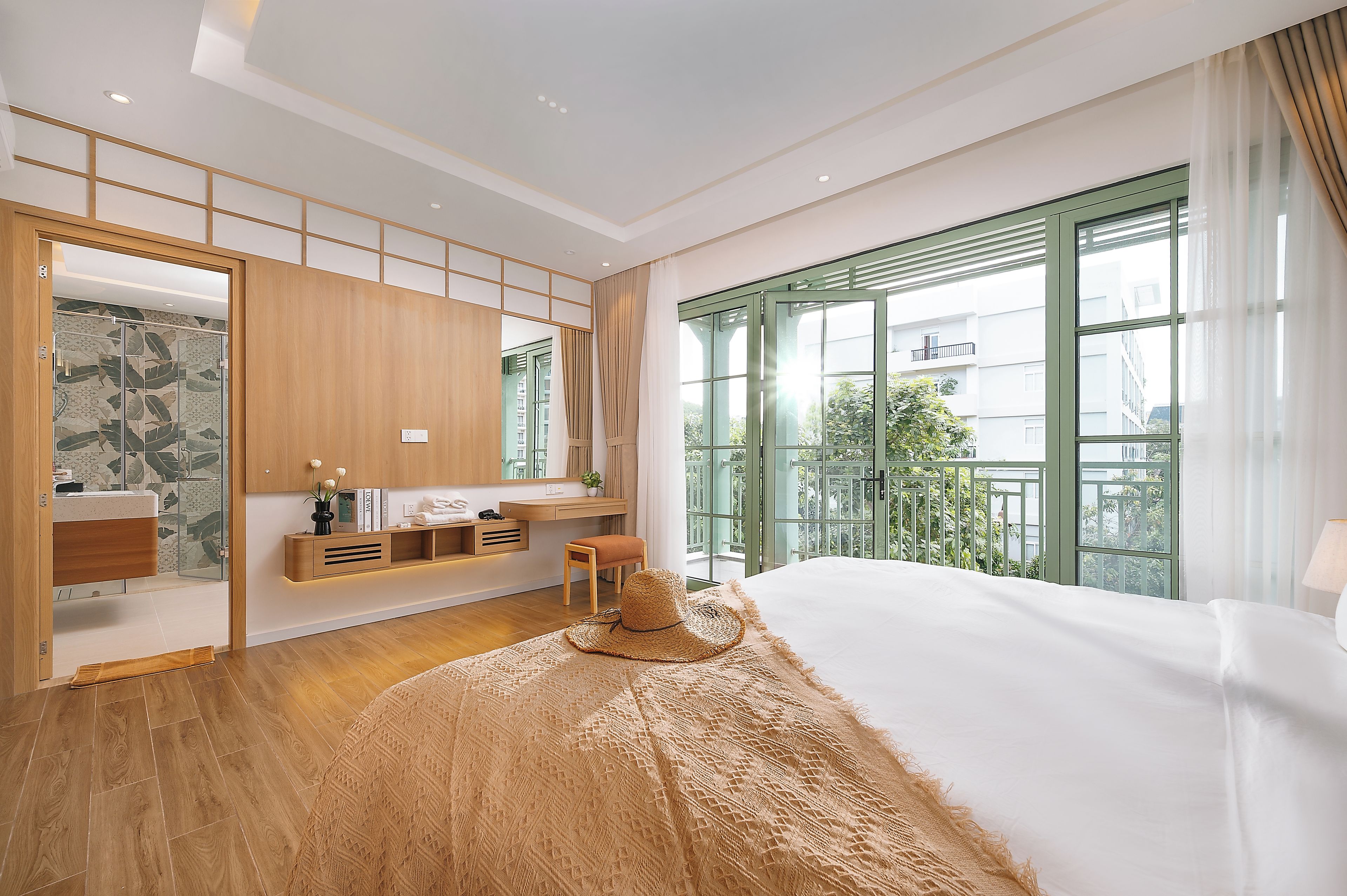 A modern bedroom with a large bed, a desk, a chair, and a view of the outdoors through a large window.