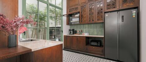 A kitchen with wooden cabinets, a stainless steel refrigerator, and a window with a view of bamboo outside.