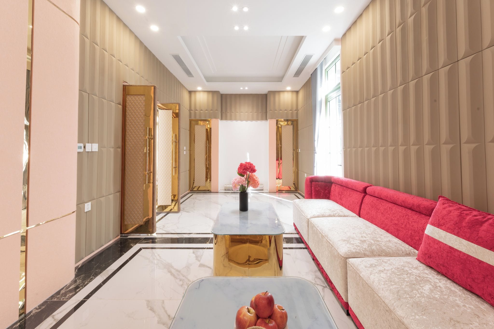 Un interior moderno con suelo de mármol, un sofá rojo, una mesa de centro dorada y un espejo que refleja la habitación.