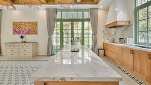 A spacious kitchen with a large island, wooden cabinets, and a view through green-framed windows. - Elyday Villa - Bai Khem Beach, Phu Quoc (Phu Quoc)