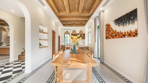 A spacious dining area with a wooden table and chairs, a vase with yellow flowers, and a wall art piece. - Elyday Villa - Bai Khem Beach, Phu Quoc (Phu Quoc)