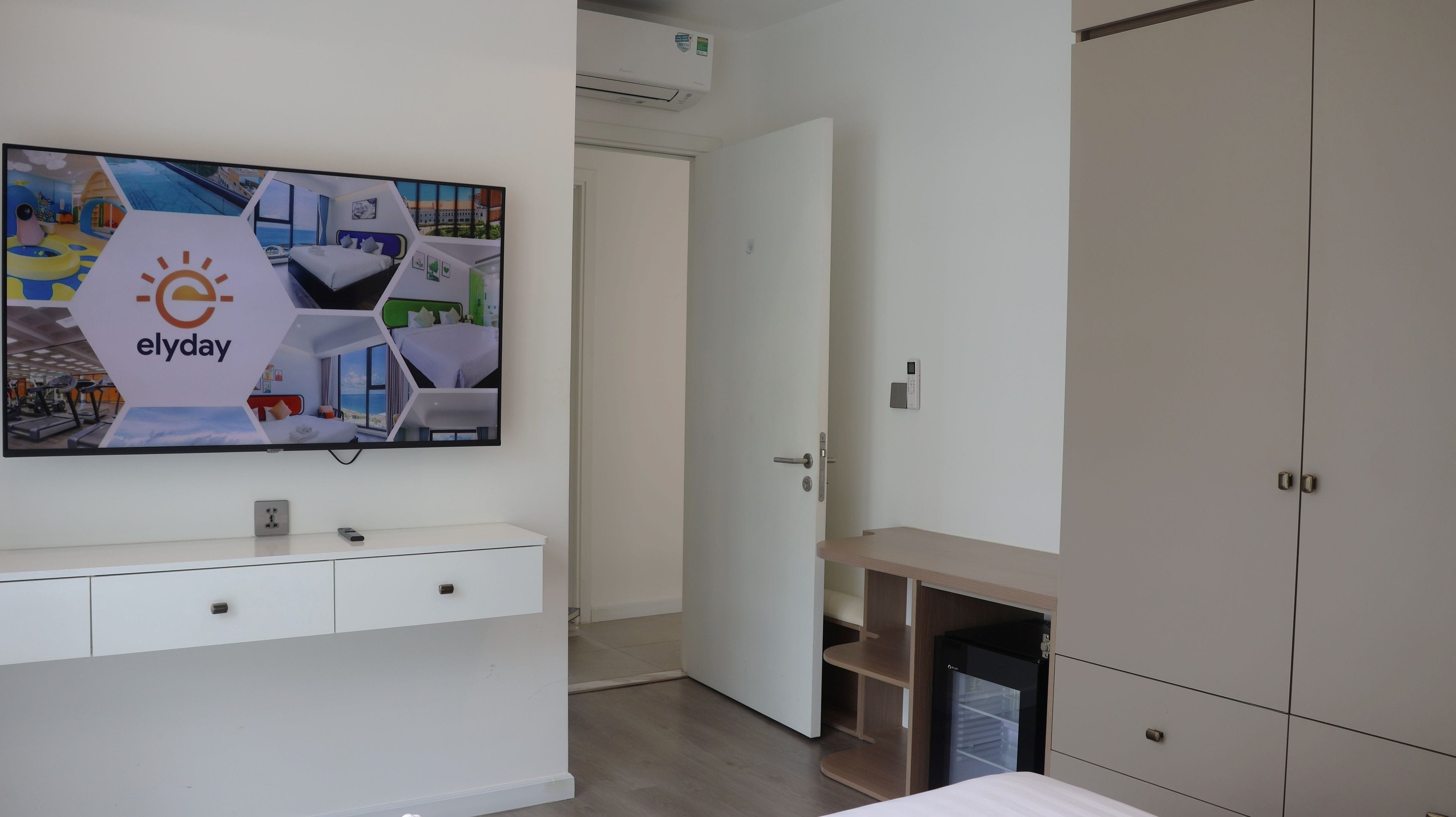 Hotellihuone, jossa on sänky, televisiossa näkyy hotellin mainos, huoneessa on vaatekaappi ja pieni työpöytä.