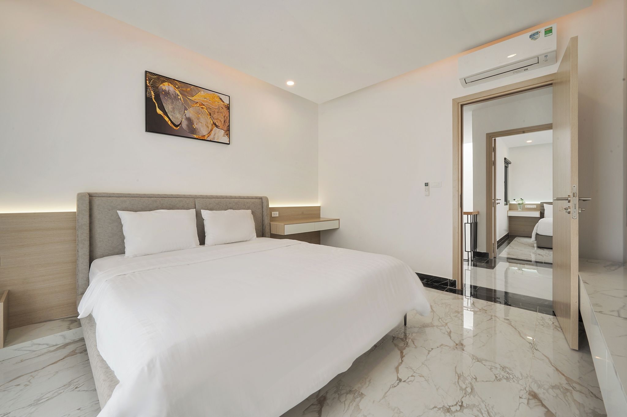 Una habitación de hotel moderna con una cama grande, una mesita de noche, un aire acondicionado y un cuadro en la pared.