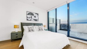 A bedroom with a bed, nightstands, a lamp, a painting, and a balcony with a view. - StayAU Spacious 2BR Stunning Sunset Views (Box Hill)