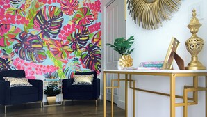 Una habitación con un llamativo mural floral, un espejo con marco dorado y una consola decorada con objetos ornamentales.