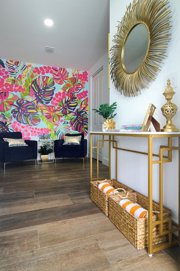 Una habitación con un llamativo mural floral, un espejo con marco dorado y una consola decorada con objetos ornamentales.