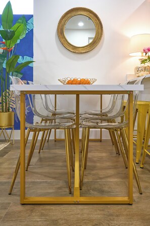 Un coin repas avec une table blanche, des chaises transparentes et un miroir encadré d’or.