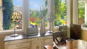 Una cucina con tavolo da pranzo, due lampade a sospensione e vista su un giardino attraverso ampie finestre.