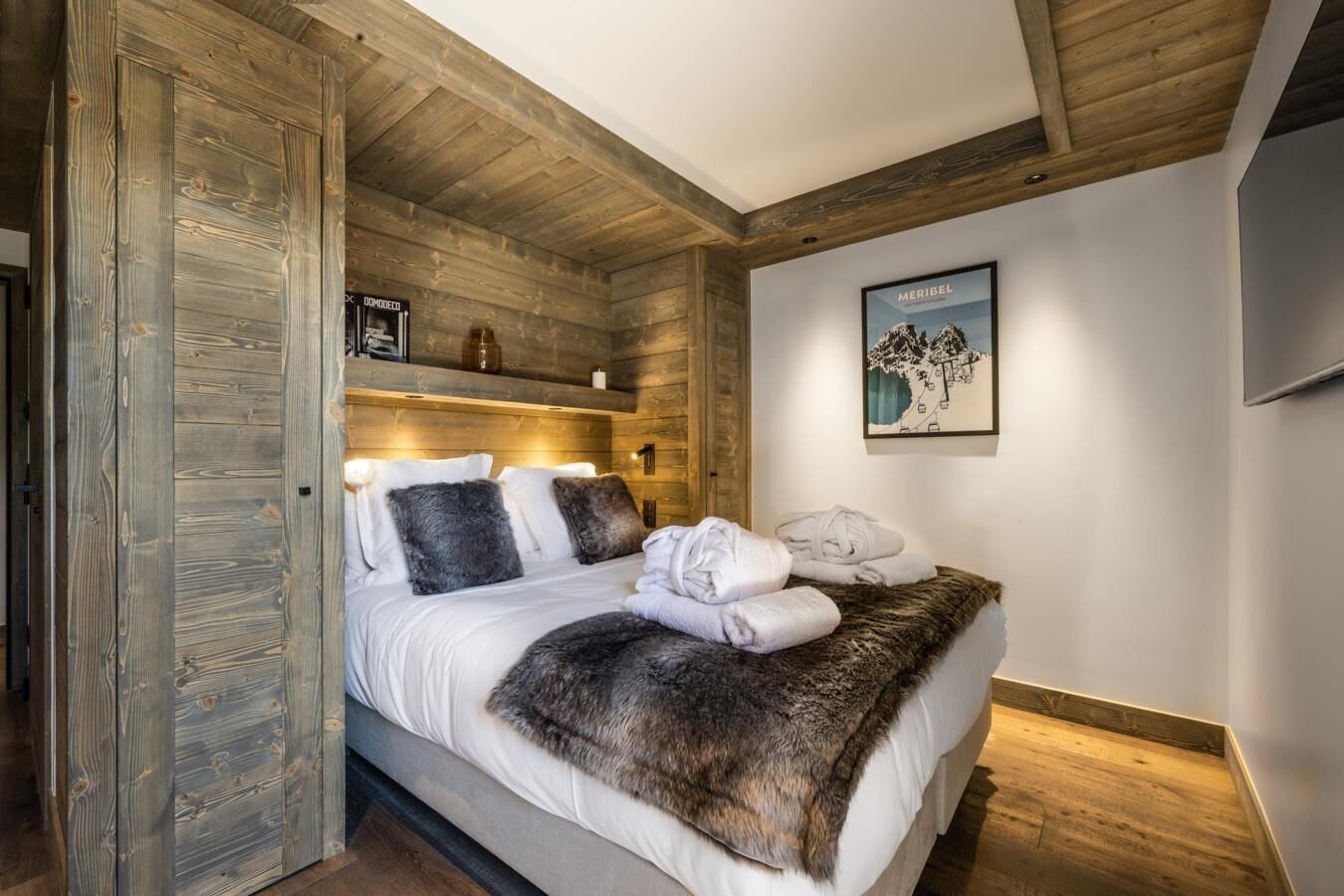 A bedroom with a wooden ceiling, a bed with white linens, a fur throw, and a framed picture on the wall.