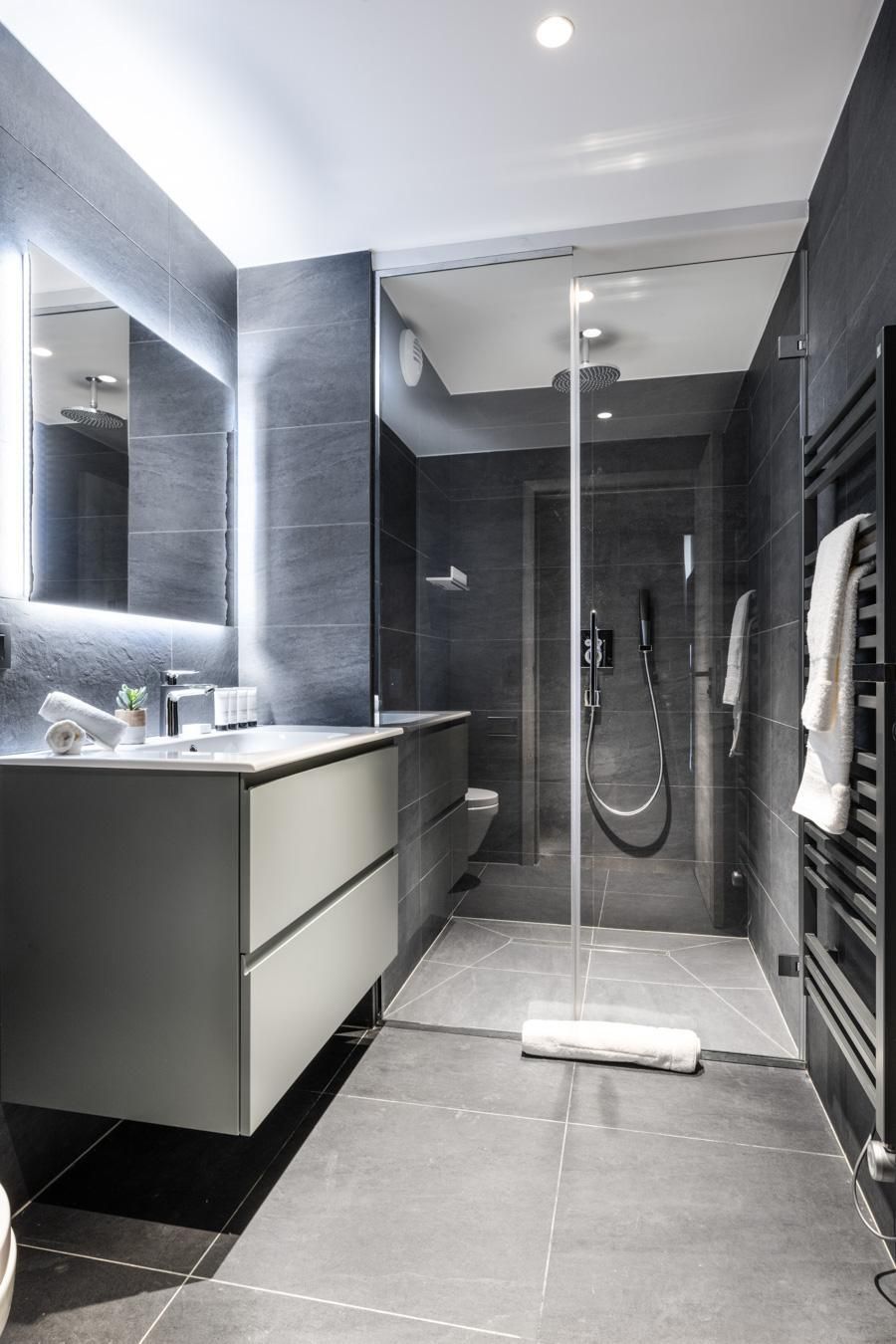 Een moderne badkamer met een douche met glazen wand, een grote spiegel en een donkere wastafelmeubel.