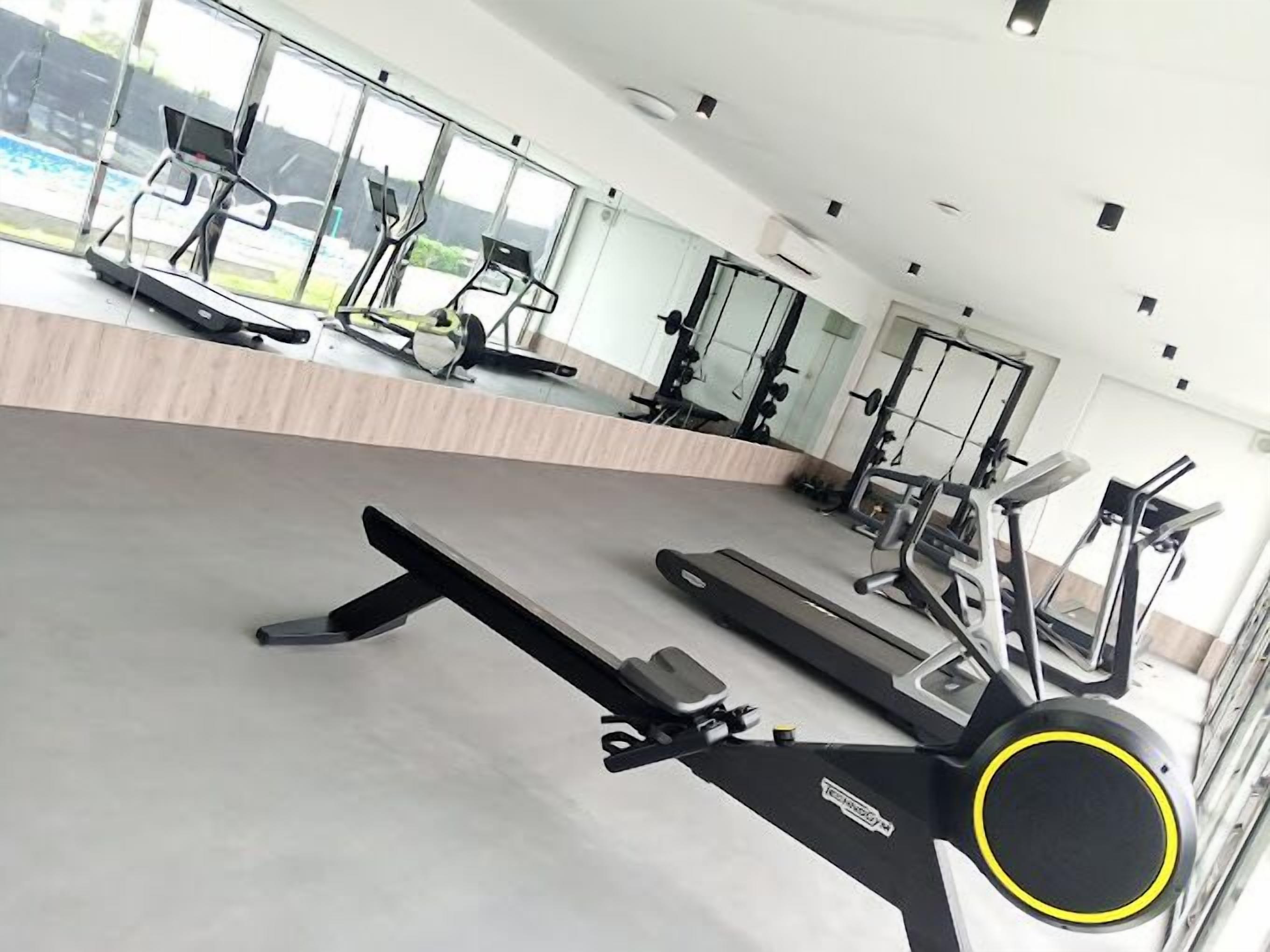 Un gimnasio con máquinas de cardio, estaciones de pesas y un espejo grande que refleja los equipos.