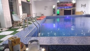 Ein Schwimmbecken mit Fliesenrand, ein Glas weißes Getränk und eine Bar im Hintergrund.