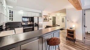 A modern kitchen with white cabinets, stainless steel appliances, and a wooden ceiling.