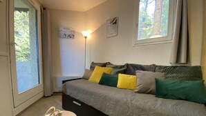 A cozy bedroom with a bed, a bedside lamp, a small table with a lamp, and a window with curtains.