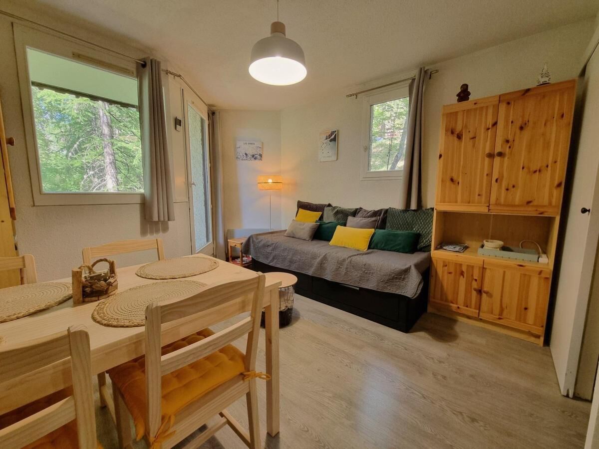 A cozy room with a wooden dining table, chairs, a bed with a gray and green bedspread, and a wooden cabinet.