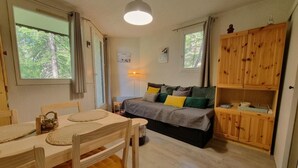 A cozy room with a wooden dining table, chairs, a bed with a gray and green bedspread, and a wooden cabinet.