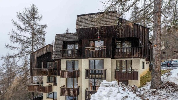 A multi-story wooden building with balconies, situated in a snowy landscape.
