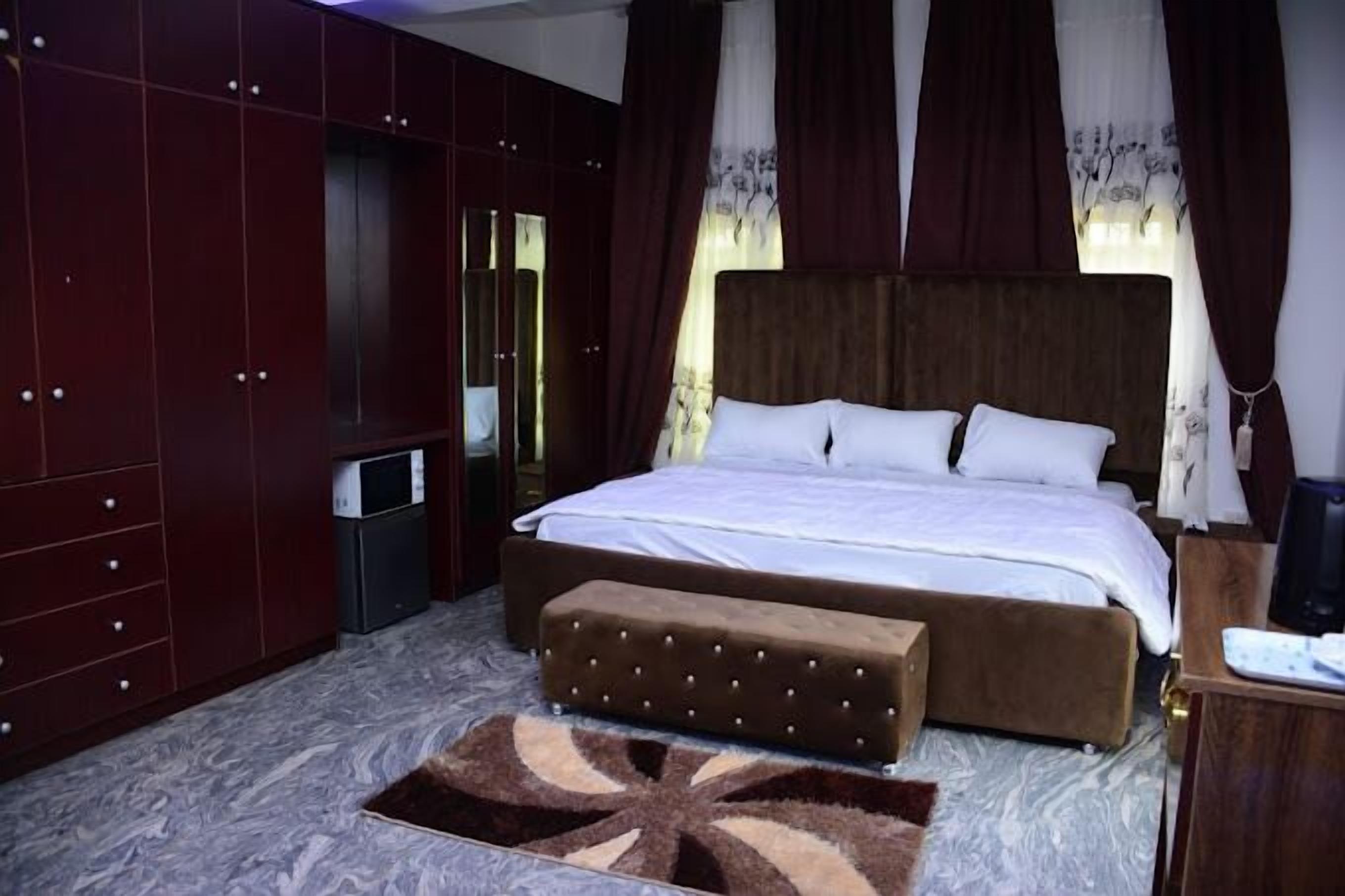 Un dormitorio con una cama grande, un armario de madera, una mesita pequeña y un banco.