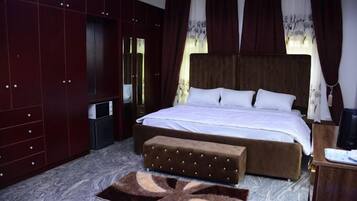 Un dormitorio con una cama grande, un armario de madera, una mesita pequeña y un banco.