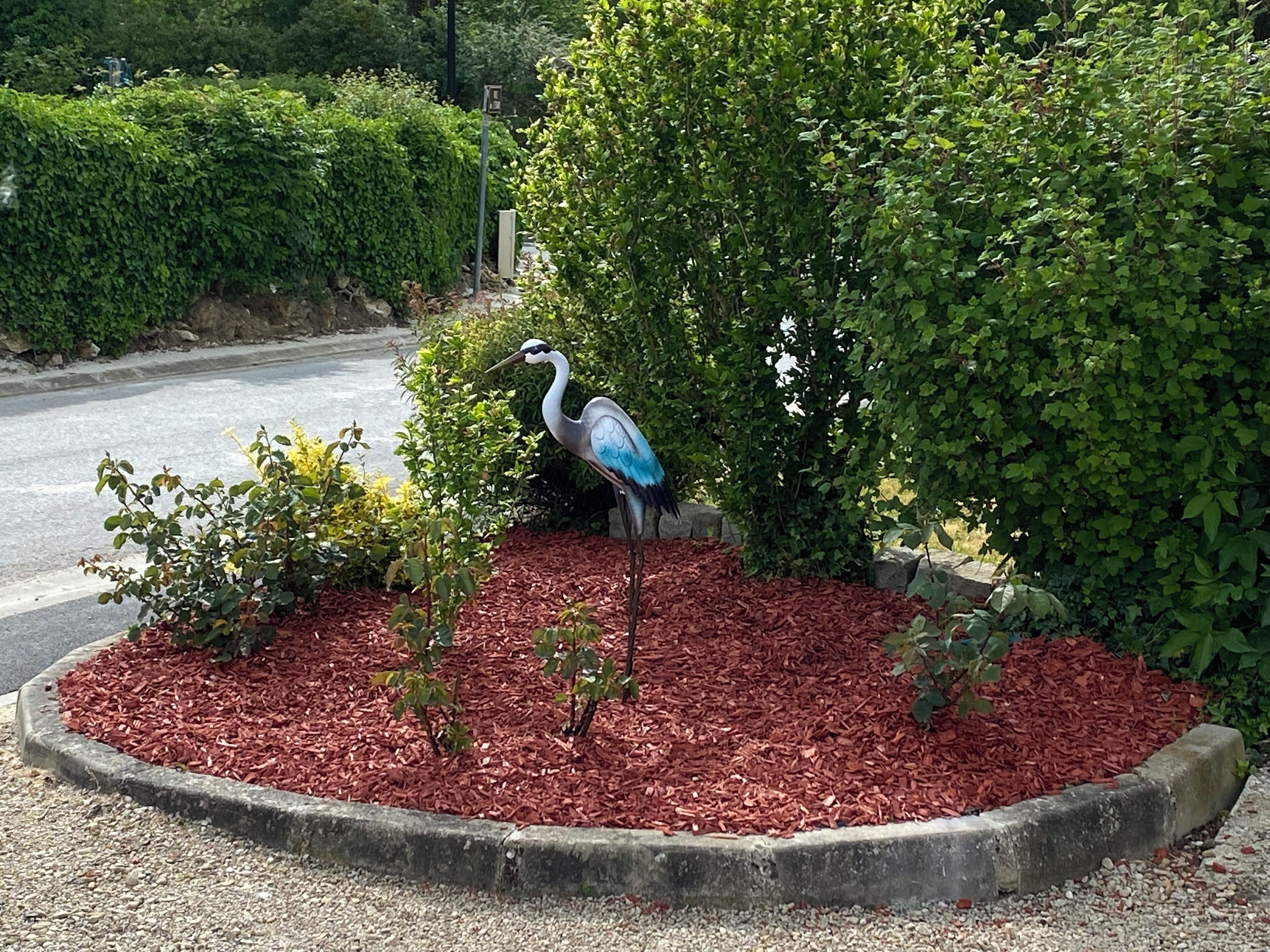A bird statue in a landscaped area with mulch and greenery.