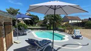 Un patio trasero con piscina, sillas de descanso y sombrillas.