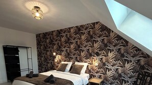 Un dormitorio moderno con una cama grande, un tragaluz, una pared con un diseño de hojas tropicales y una mesita de noche pequeña.