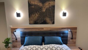 A bedroom with a bed, two wall-mounted lights, a wall art piece, and a nightstand with a plant.