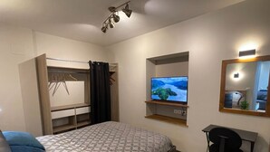 A bedroom with a bed, a desk, a TV, a mirror, and a wardrobe.