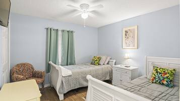 A bedroom with a bed, a chair, a nightstand, a ceiling fan, and a window with curtains.