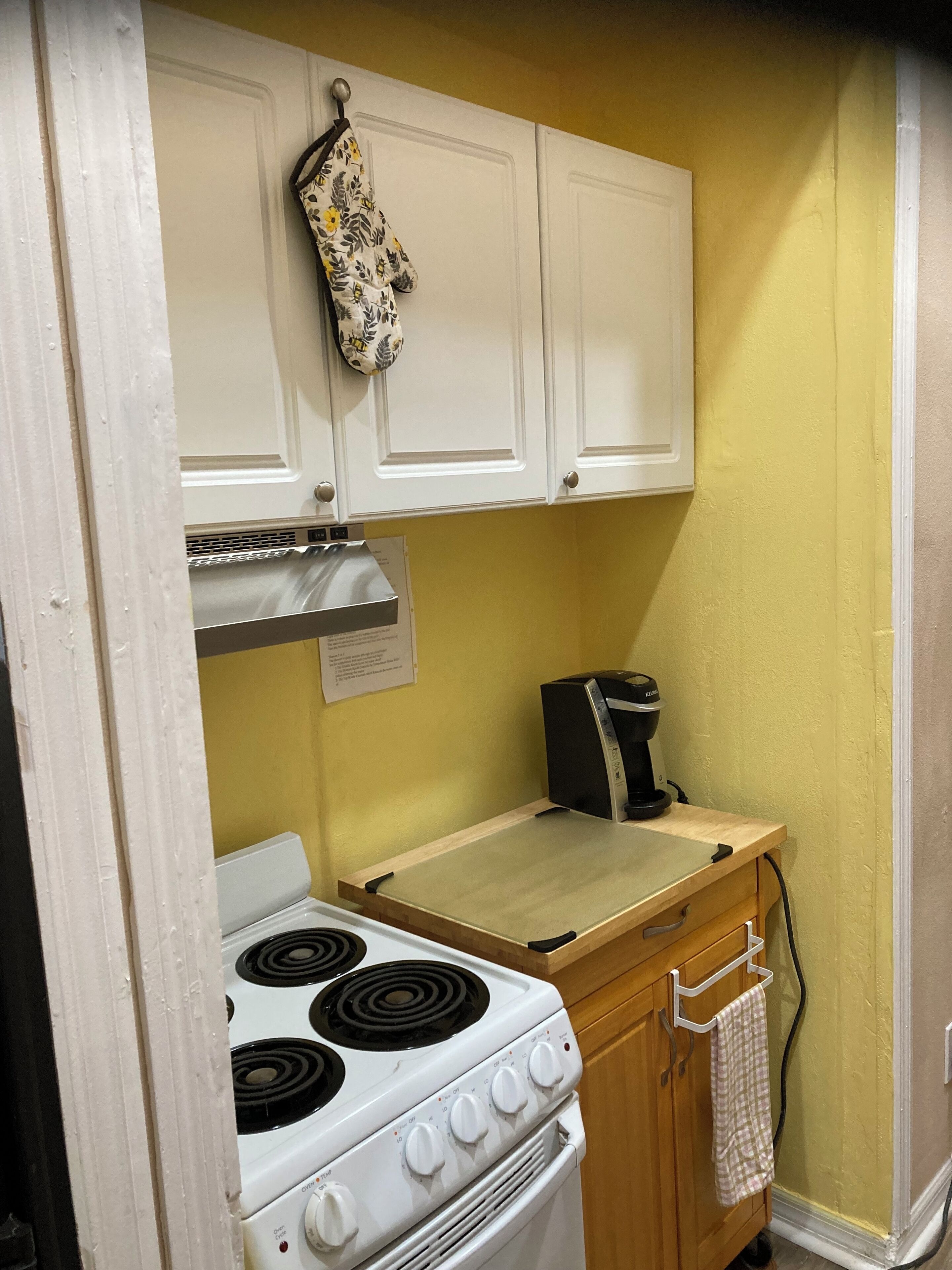A compact kitchen with white cabinets, a stove, and a coffee maker.