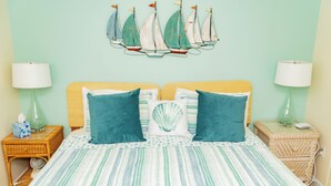 Ein Schlafzimmer mit gestreifter Bettdecke, zwei Kissen, einer Wanddekoration mit Segelboot und zwei Nachttischen mit Lampen.