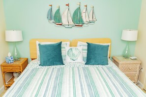 A bedroom with a striped bedspread, two pillows, a wall-mounted sailboat decoration, and two bedside tables with lamps.