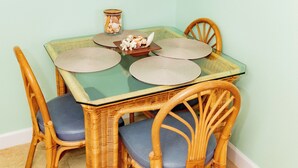 A dining area with a glass-top table, wicker chairs, and a framed picture of a beach scene. - #306 Lovers Key Beach Club (Bonita Springs)