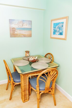 A dining area with a glass-top table, wicker chairs, and a framed picture of a beach scene.