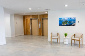 Un hall d’entrée avec deux portes en bois, un tableau représentant un paysage côtier et deux chaises en bois agrémentées d’une petite plante.