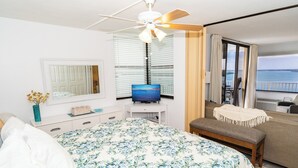 A bedroom with a bed, a TV, a bench, a window with blinds, and a view of the sea. - #803 Lovers Key Beach Club Ocean Views (Bonita Springs)