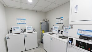 A laundry facility with multiple washing machines and dryers, control panels, and informational posters on the walls. - #803 Lovers Key Beach Club Ocean Views (Bonita Springs)