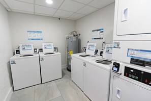 A laundry facility with multiple washing machines and dryers, control panels, and informational posters on the walls. - #803 Lovers Key Beach Club Ocean Views (Bonita Springs)