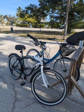 Un vélo bleu, muni d’un panier et d’une bouteille d’eau, est garé sur une surface en béton, près d’une clôture en bois.