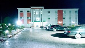 Un hotel con un amplio estacionamiento, varios autos y una entrada bien iluminada.