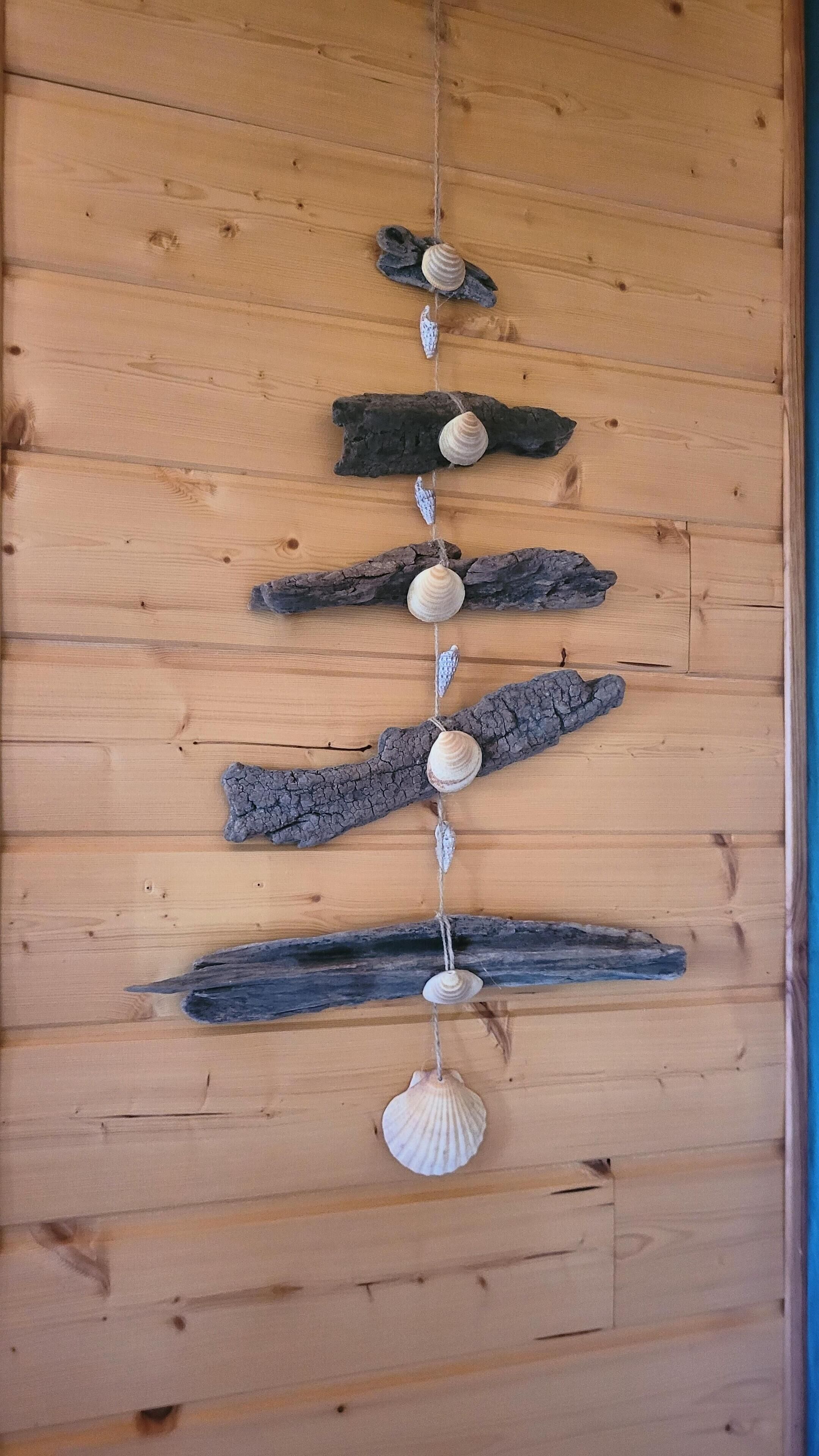Un mur en bois orné d’une guirlande de coquillages et de morceaux de bois flotté disposés à la verticale.