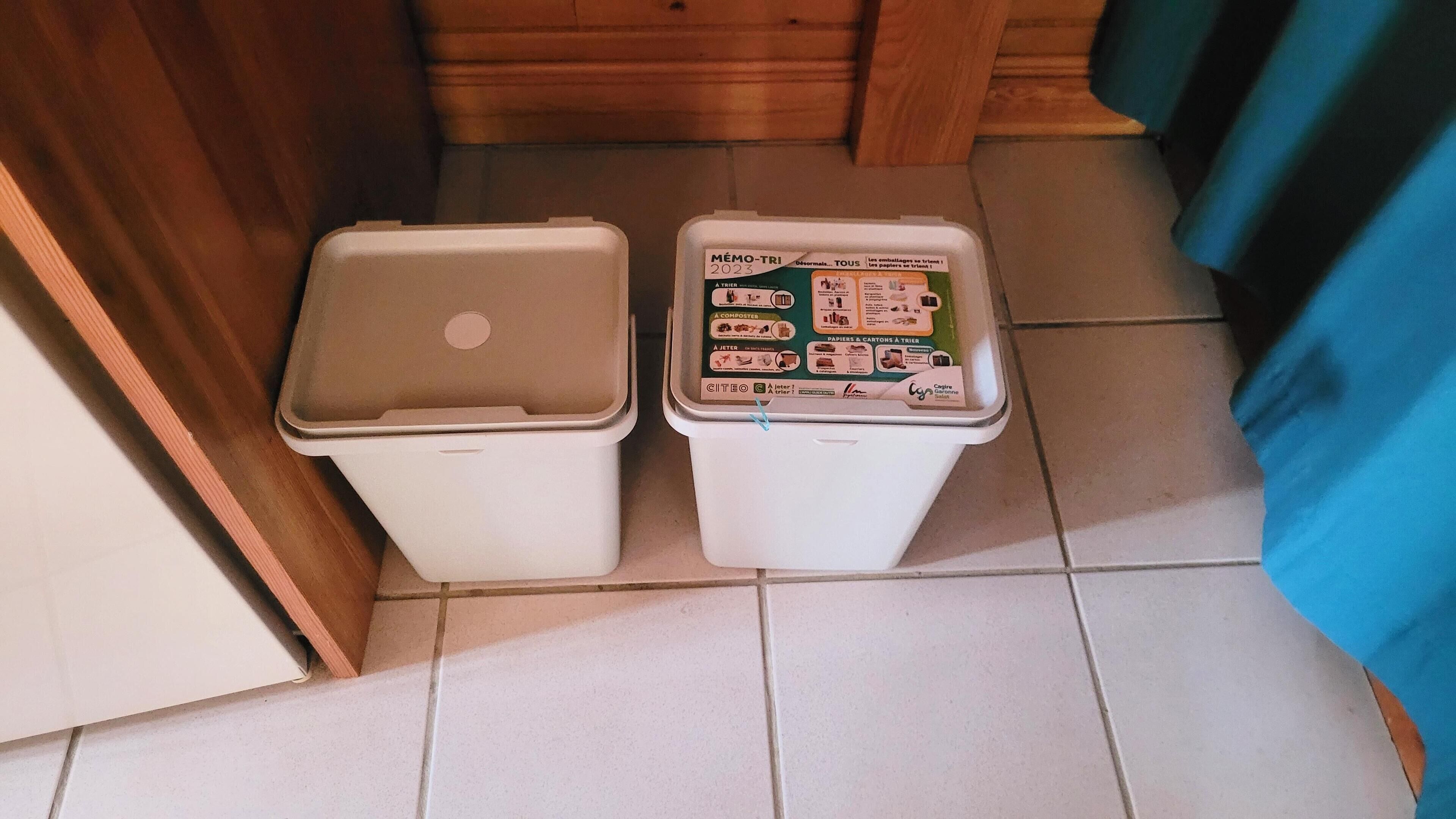 Two trash bins in a room with a tiled floor and wooden walls.