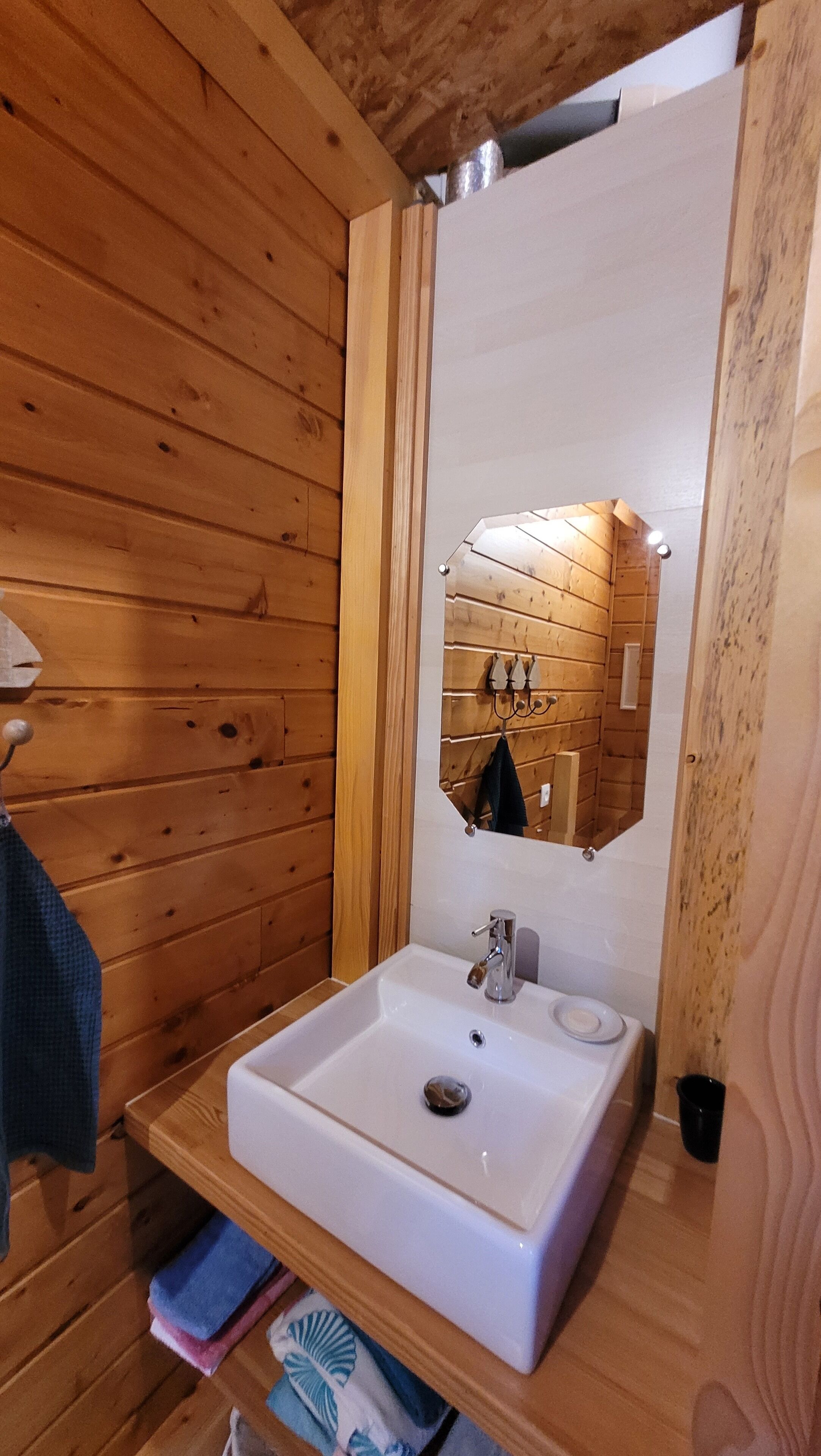 Une salle de bain rustique, avec des murs en bois, un lavabo blanc, un miroir et un porte-serviettes.