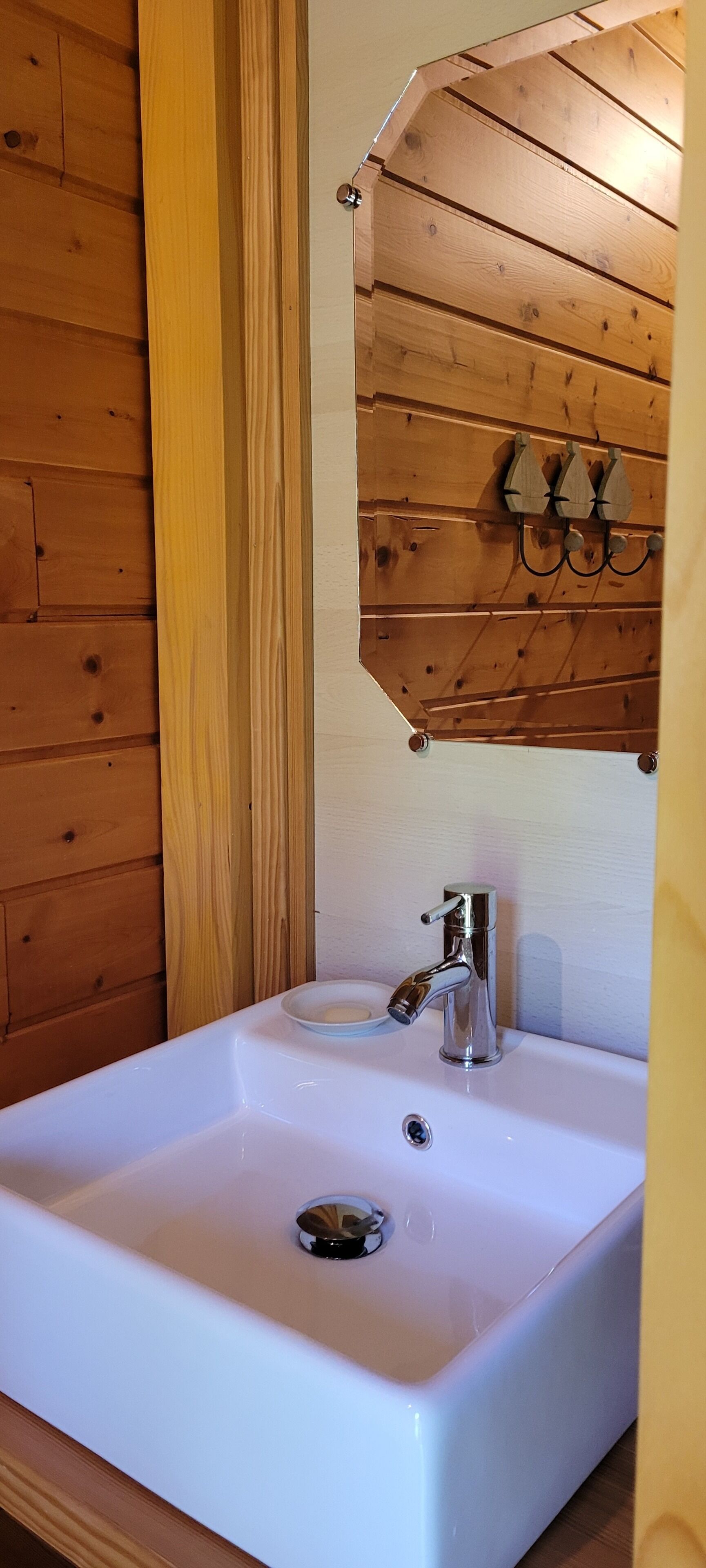 A white bathroom sink with a chrome faucet, a soap dish, and a wooden wall panel above.