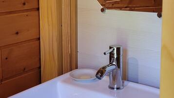 A white bathroom sink with a chrome faucet, a soap dish, and a wooden wall panel above.