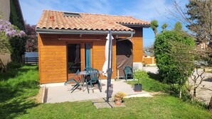 A small wooden house with a tiled roof, a patio with chairs, and a small garden. - Reflet de Bien être : Wooden loft for 3 people with enclosed courtyard. (Marsoulas)
